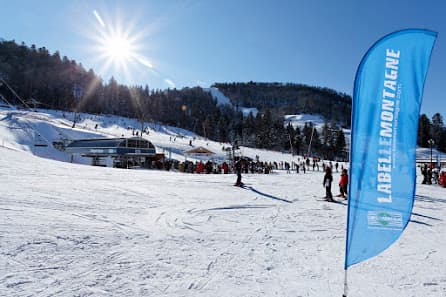 Winter sports enthusiasts enjoying their time at La Bresse-Hohneck ski resort in Vosges, France, with skiers on the slopes and a cozy chalet nearby.