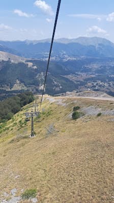 A ski lift against a snowy backdrop in Pescasseroli Italy. A challet is also visible in the distance. A skier readies to descend and a mountain can be faintly seen. The setting is truly a picturesque ski resort.