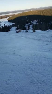 A skier gliding down the slopes at Smokey Mountain ski resort in Labrador City Canada. The scene is wintery with a ski lift in the background and a hint of a snowmobile nearby.