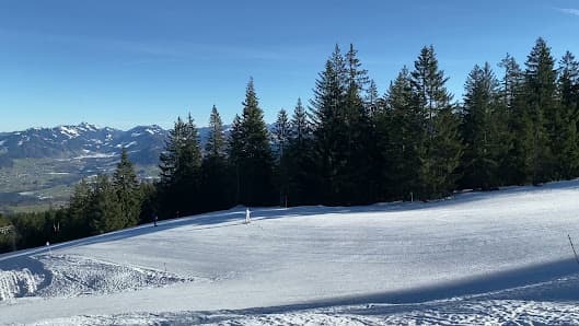 A winter sports scene at Bödele, Bregenz in Austria, featuring a skier gliding down the snow covered slopes of a ski resort with a charming chalet and scenic mountain backdrop.