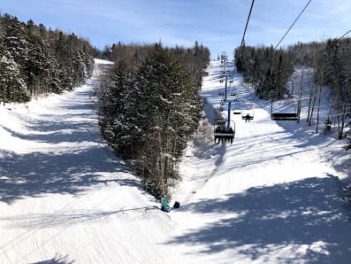 A bustling winter scene at Poley Mountain ski resort in Waterford NB Canada. Active skiers enjoy crisp slopes as a ski lift hums in the background near a quaint challet.