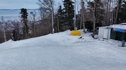 A skier and snowmobile are enjoying a winter sports scene at Sljeme in Zagreb Croatia. There is a ski lift in the background and a chalet nearby on this snowy day.