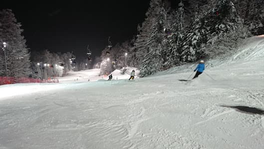 A vibrant winter sports scene at Sljeme Zagreb featuring a skier gliding down the slopes of a ski resort. Visible elements include a ski lift tracked slopes and a cozy chalet in the backdrop.
