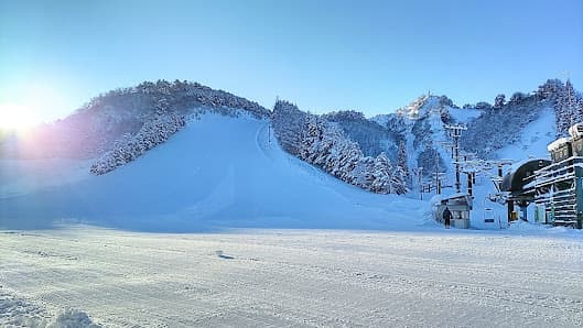 Snow-clad mountain in Tainai, Japan, hosting a bustling winter sports scene. A ski resort peeks through the visually captivating winter panorama, with a snowmobile adding to the lively vibe.