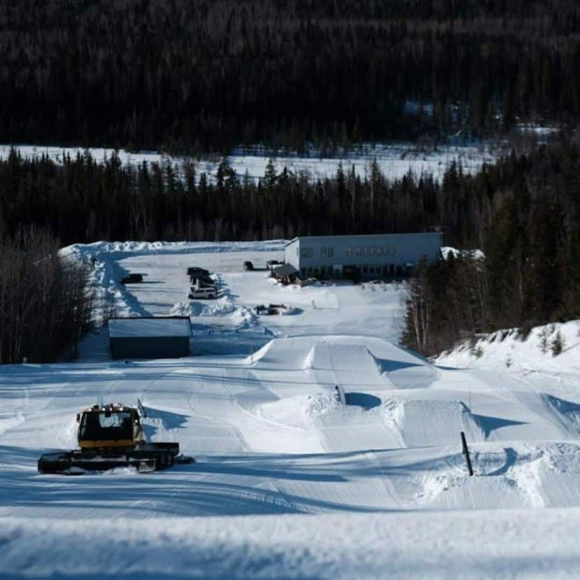 Winter sports scene at Murray Ridge in Fort St James, British Columbia showcasing a bustling ski resort surrounded by pristine snow, a distant skier, and a parked snowmobile.