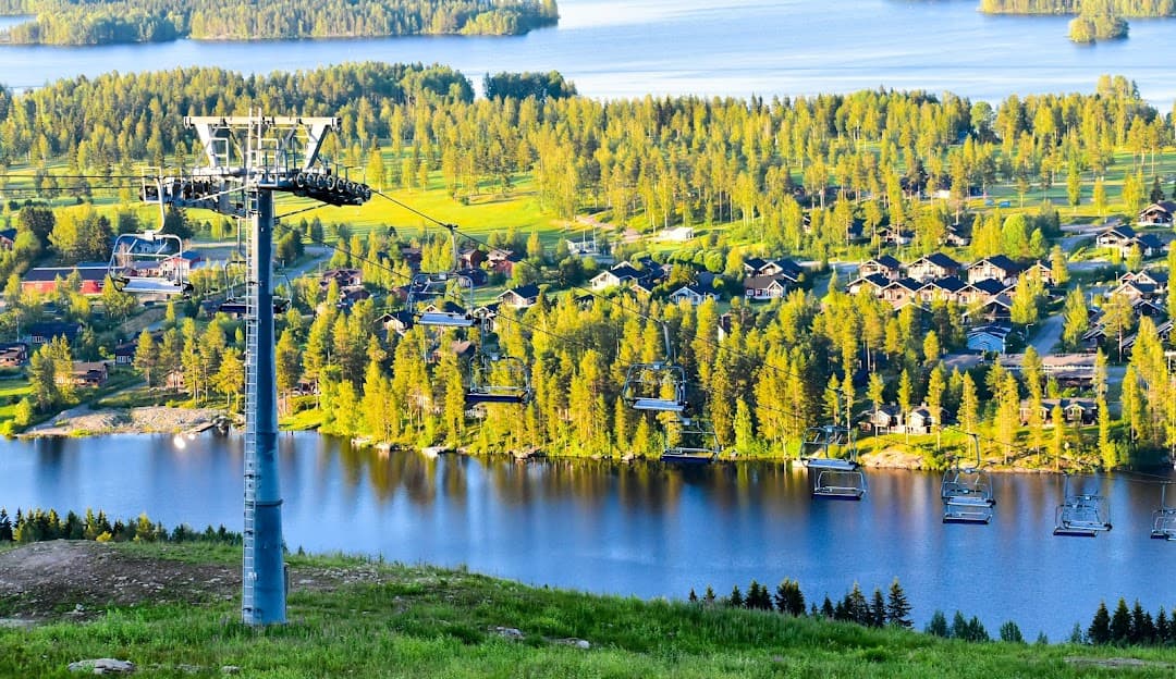 A ski lift ascending at the Tahko resort in East Finland with a skier prepping for a descent. The snowy scene punctuated by a lake speaks to the beauty of winter sports in the region.