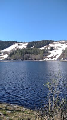View of the serene Tahko Lake in Kuopio, East Finland, surrounded by a popular ski resort. A quaint chalet overlooks the winter sports scene against a majestic mountain backdrop.
