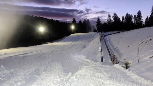 Winter scene at Cloudcroft, New Mexico showcasing a bustling ski resort complete with a lively sports center, a picturesque challet, and a ski lift against a backdrop of snow-covered slopes.