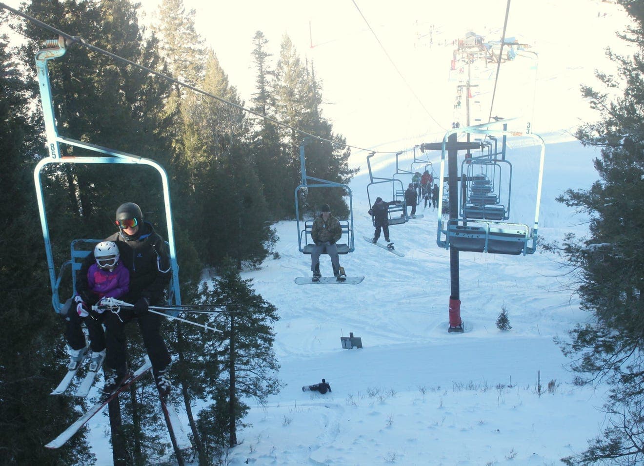 A view of Cloudcroft New Mexico showcasing a bustling winter sports scene at a ski resort. Visitors traverse the snowy slope using a ski lift while a skier makes their descent. A cozy chalet is also visible nearby.