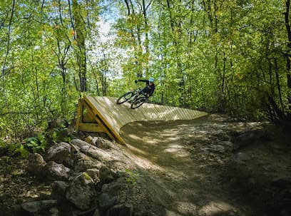 A biker embarking on a thrilling ride through the stunning green landscapes of Mont Rigaud in Quebec Canada. His journey is marked by a small challet nestled in the distance.