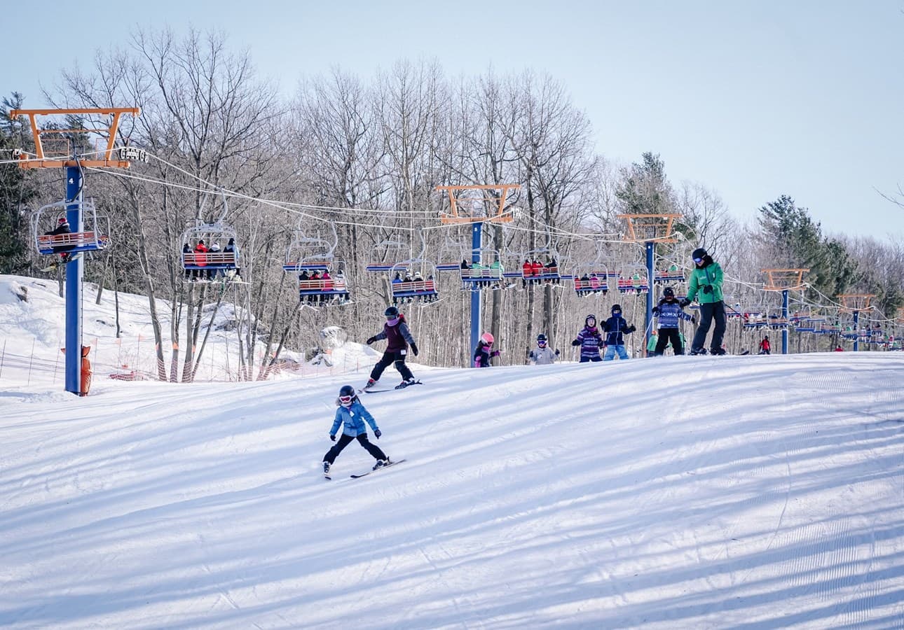 A vibrant winter sports scene at Mont Rigaud in Quebec, Canada, showcasing lively skiers enjoying their runs, amidst picturesque snow-covered slopes.