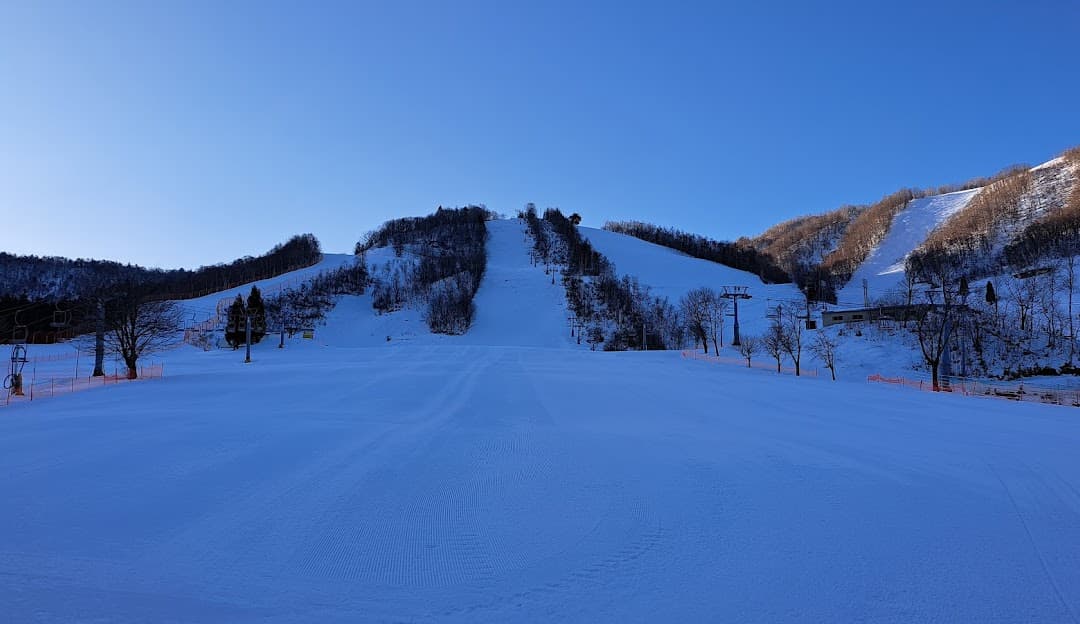 View of Honokidaira ski resort in Takayama, Honshu, Japan featuring a scenic winter landscape, an active ski scene with skiers, a chalet, and a ski lift amidst snow-covered mountains and clear skies.