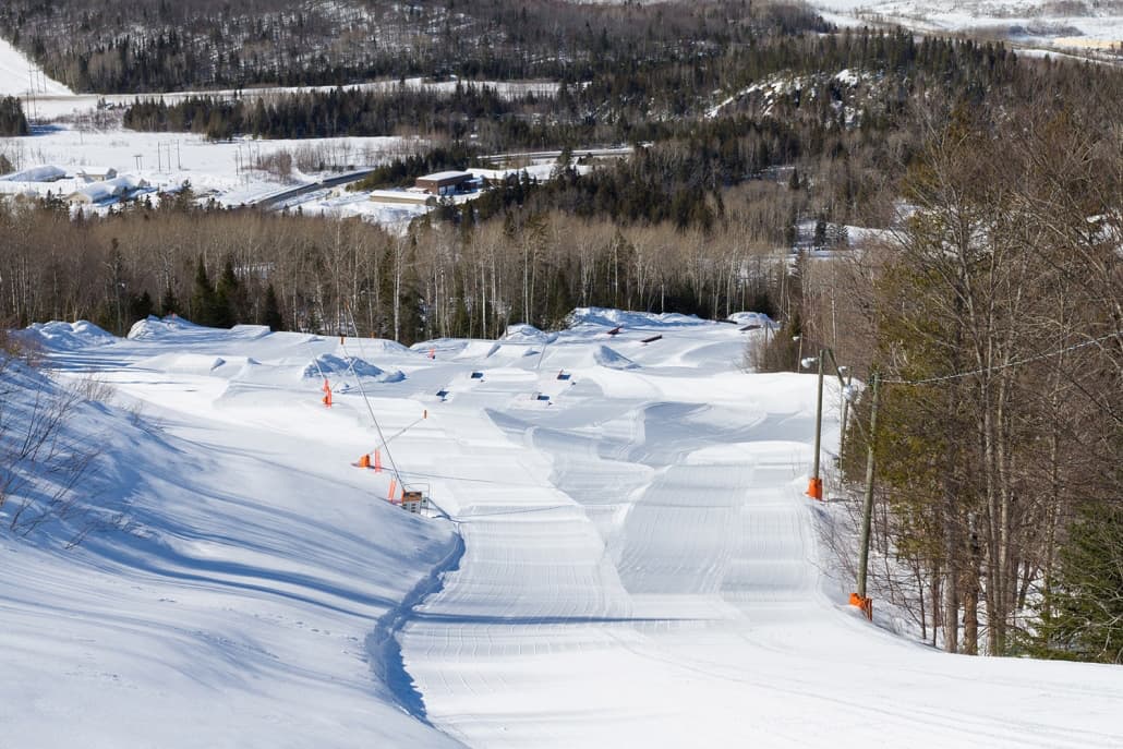 Winter scene at Sugarloaf Provincial Park in Atholville, New Brunswick, Canada showcasing a bustling ski resort. The landscape is dotted with skiers enjoying the snow-covered slopes.
