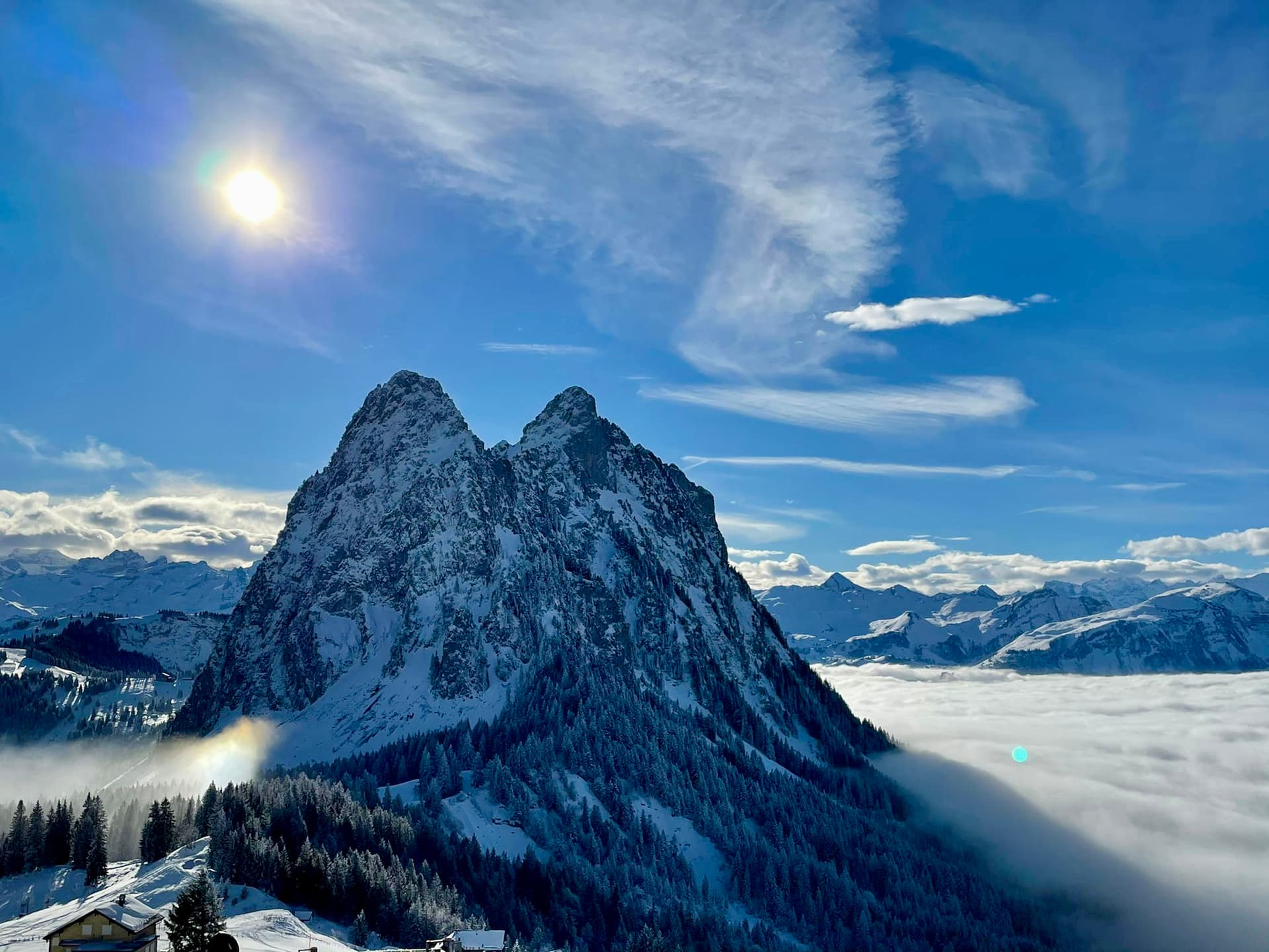 A scenic view from Brunni-Bahnen in Engelberg, Switzerland featuring a rugged mountain partially covered in snow, a cozy chalet, and an active winter sports scene.