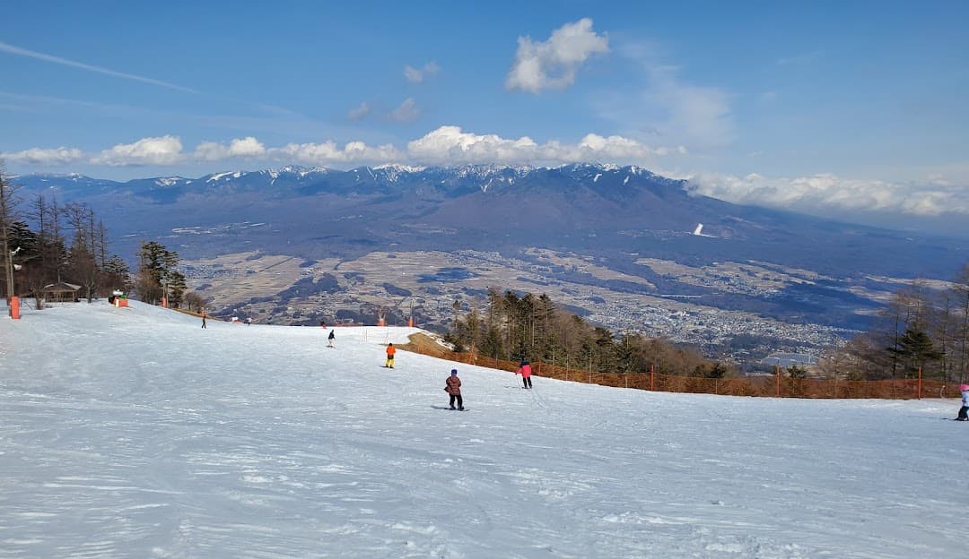 Winter sports enthusiasts at Fujimi Panorama ski resort in Chūbu, Japan. Skiers descend slopes peppered with chalets against a beautiful snowy backdrop.