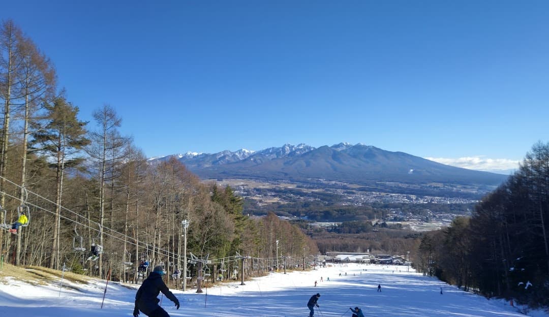 Winter scene at Fujimi Panorama ski resort in Nagano, Japan, featuring snow-covered mountains in the backdrop, a charming chalet, and skiers enjoying the slopes.
