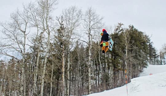 A snowboarder setting off on a thrilling ride at the snowy Loch Lomond hills in Thunder Bay, Ontario, Canada. The pristine white snow under clear skies provides an ideal setting for winter sports.