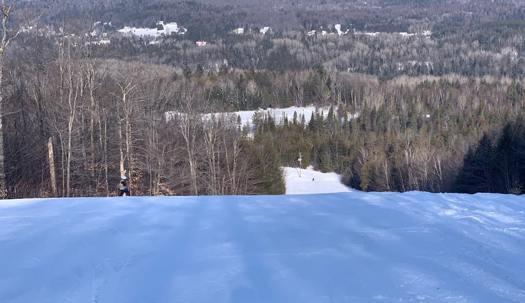A skier glides down a snowy slope at the Montcalm ski resort in Rawdon Quebec. The winter sports scene is complete with a distant mountain backdrop and a nearby ski lift.