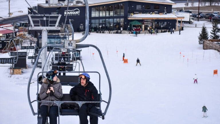 The photo shows a vibrant winter sports scene at Bousquet ski resort in Pittsfield Massachusetts featuring a ski lift a skier and a snowmobile amidst a snowy landscape.