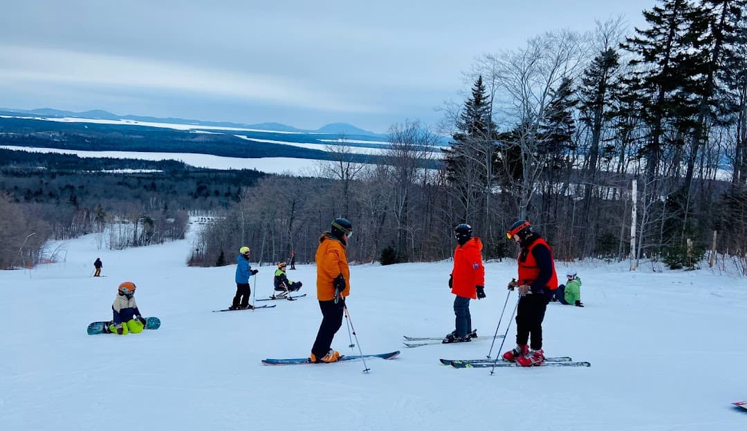 Skiers enjoying winter sports at Big Moose Mountain in Greenville Junction, Maine, USA. The snow-covered slopes are alive with activity as a family and other groups glide down the mountain.