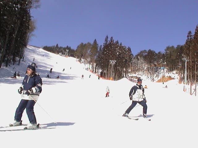 View of the Megahiraonsen Megahira Ski Area in Hiroshima, Japan, featuring a chalet and winter sports with the visible skier descending the slope.
