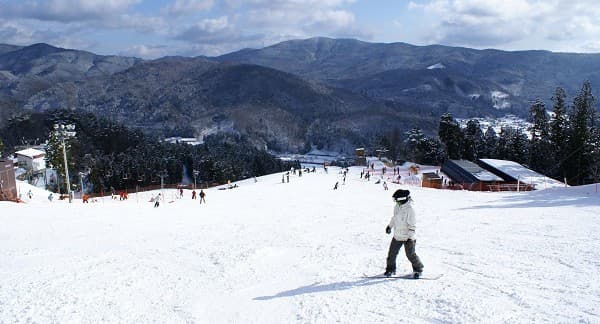 Winter scene at Megahiraonsen Megahira Ski Area in Hiroshima, Japan featuring a ski resort, a chalet, and a skier amid breathtaking winter scenery.