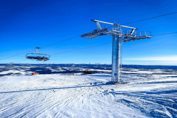 A picturesque view of Golsfjellet in Norway featuring a ski lift at a ski resort. Various skiers engage in winter sports amidst the serene snow-blanketed landscape. A small chalet is visible in the distance.