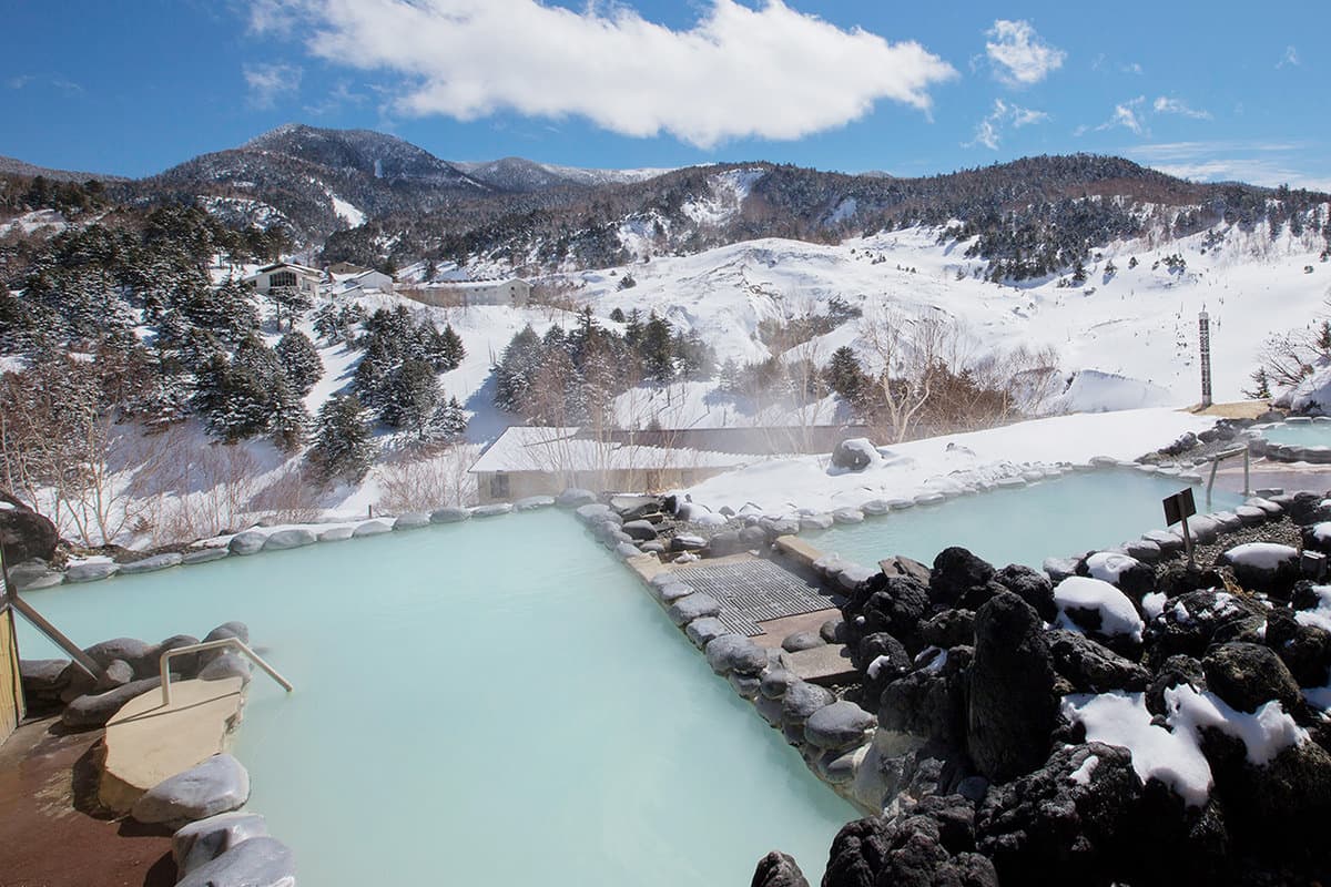 Manza Onsen in Japan - a body of water surrounded by snow covered mountains.