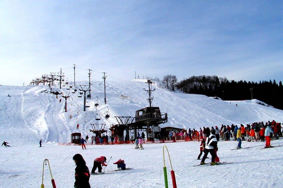 A winter sports scene in Itsukamachi, Niigata, Japan. Features prominently a ski resort with a ski lift in the background, amidst a backdrop of pristine snow-covered slopes.