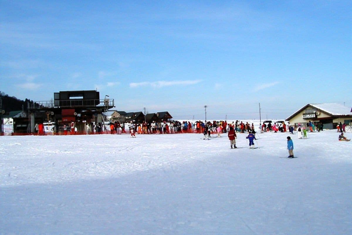 A busy winter scene at Itsukamachi Ski Resort in Niigata Japan featuring multiple skiers navigating the snowy terrain complete with a ski centre and chalet in the background.