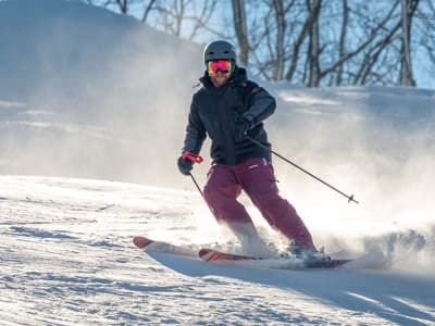 A skier enjoying a winter sports scene at Ober Mountain in Gatlinburg Tennessee. The ski resort is bustling with activity; snowboarders and groups of skiers spotted across the snowy landscape.