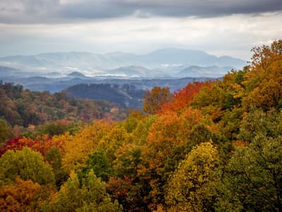 A picturesque winter scene at Ober Mountain Gatlinburg Tennessee showcasing a stunning mountain range adorned with lush forests. A charming chalet overlooks the snowy landscape where winter sports are taking place.