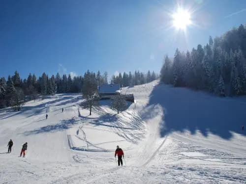 Winter scene at Ventron ski resort in Vosges, France featuring an snowy landscape with a skier on a trail and a ski lift in the background.