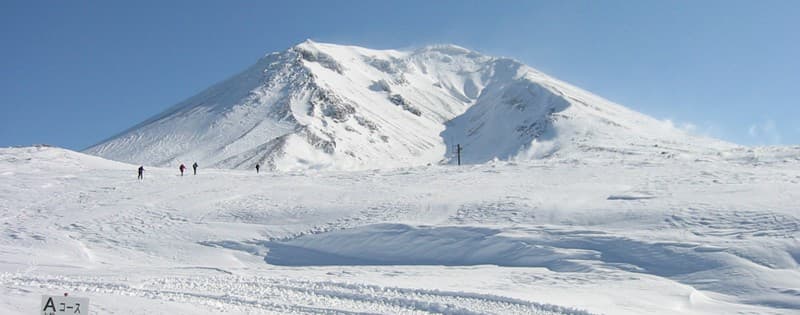 Asahidake in Japan - a group of people skiing down a snow covered mountain.