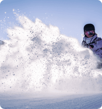 A lively winter sports scene at Peyragudes in France featuring a skier and a snowboarder navigating the snowy slopes. A snowmobile is also visible with a chalet nearby showcasing the quintessential alpine adventures in Hautes-Pyrénées.