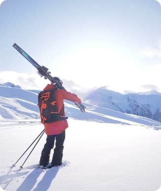 A skier descends a crisp winter slope in Peyragudes, France with a rustic chalet and bustling winter sports centre in the backdrop.