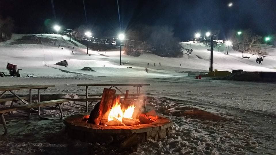 View of Seven Oaks ski resort in Iowa, USA, showcasing a tranquil winter sports scene. Skiers can be spotted, enjoying the well-maintained slopes and ski lift.