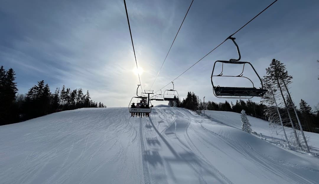 Winter sports enthusiasts at Brookvale Ski Park in Prince Edward Island, Canada, where a ski lift ascends a snowy peak as a skier heads downhill, a chalet visible in the backdrop.