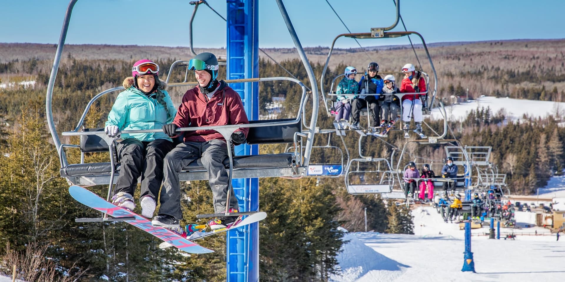 Winter scene at Brookvale Ski Park, PEI, Canada showcasing a busy ski lift and various skiers, including a family, all enjoying the snow-covered slope.