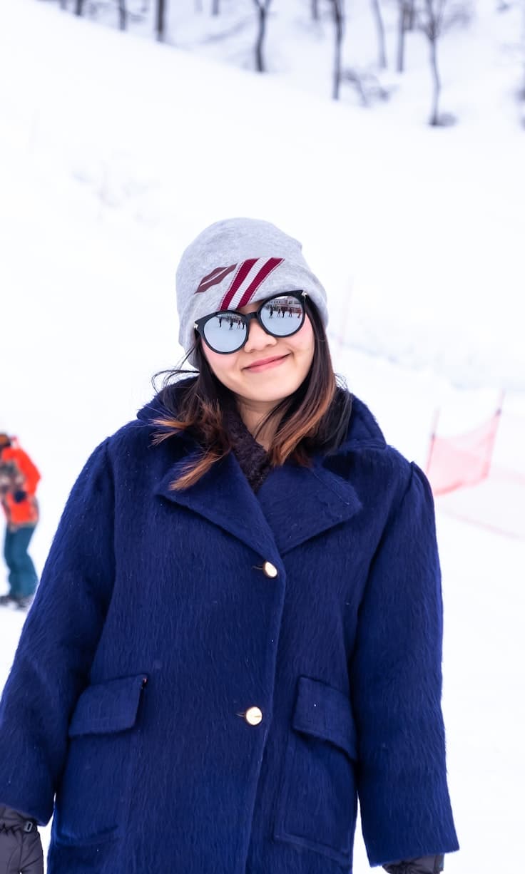 Koide in Japan - a woman standing in the snow wearing a blue coat.