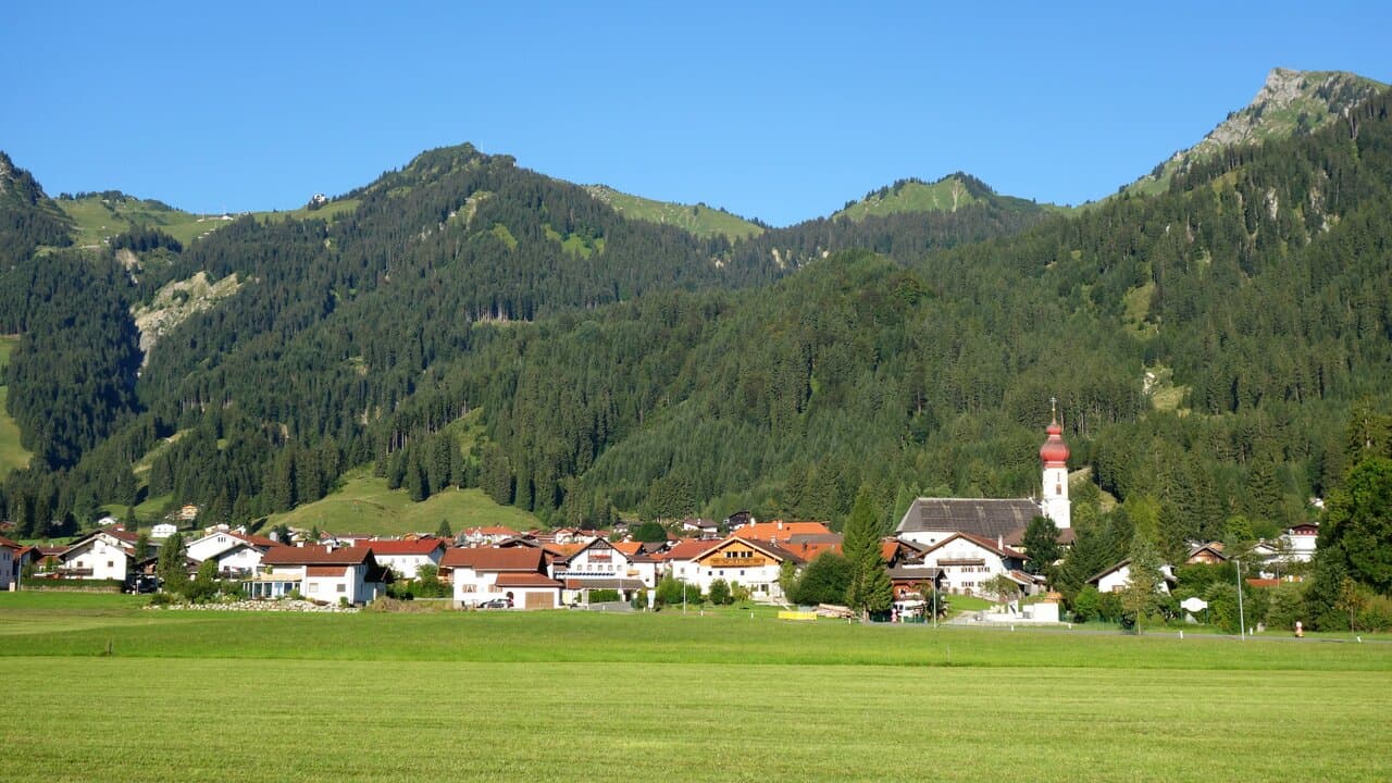 Hahnenkamm – Höfen | Reutte in Austria - a green field with houses and mountains in the background.