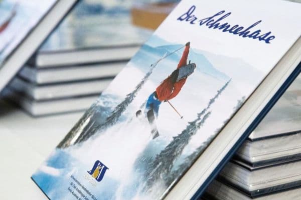 A skier making their way down a snowy slope in Hahnenkamm - Höfen | Reutte, Außerfern, Tyrol, Austria. A charming chalet and scenic winter sports scene visible in the backdrop.