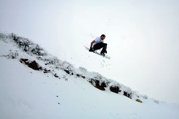A snowboarder is skillfully navigating a snowy slope in Matroosberg, Western Cape, South Africa. The vast, white landscape shimmers under sunlight, emphasizing the daring adventure.