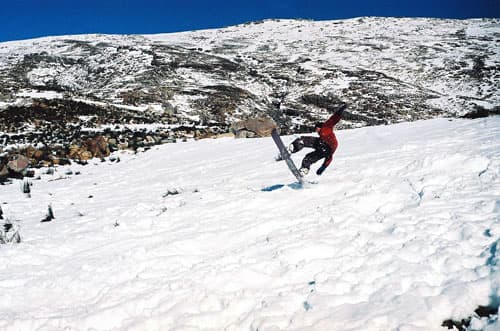 A skier and snowboarder enjoying winter sports at Matroosberg ski resort in Western Cape, South Africa, with a chalet in the backdrop.