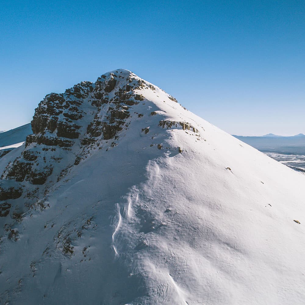 View of the peak of Matroosberg mountain in Western Cape, South Africa, partially covered in snow with a chalet in the foothills and a skier enjoying winter sports.