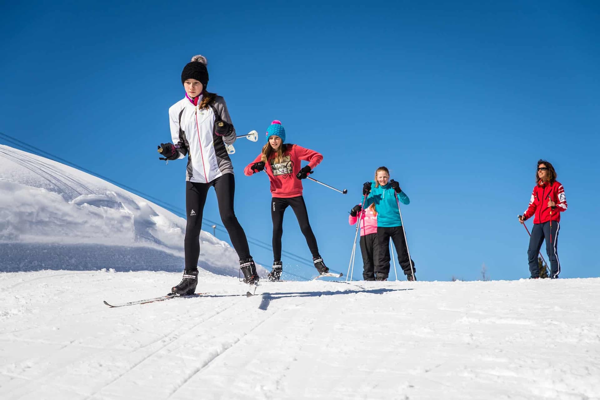 A winter sports scene in Karellis Savoie Mont Blanc France featuring a family and a group of people enjoying skiing with a winter sports centre in the background.