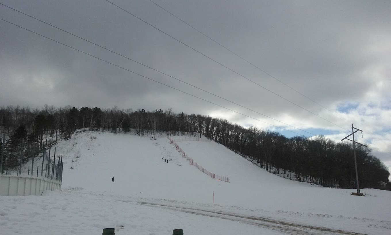 A vibrant winter scene at Pinehurst Park in Eau Claire Wisconsin showcasing a ski resort with snow-covered slopes. A skier in action enhances the lively atmosphere of this popular winter sports destination.