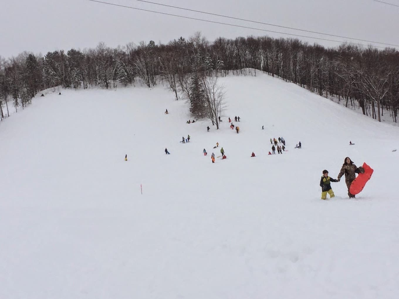 Winter sports scene at Pinehurst Park, Eau Claire, Wisconsin, featuring bustling activity at a ski resort with skiers and a ski lift.
