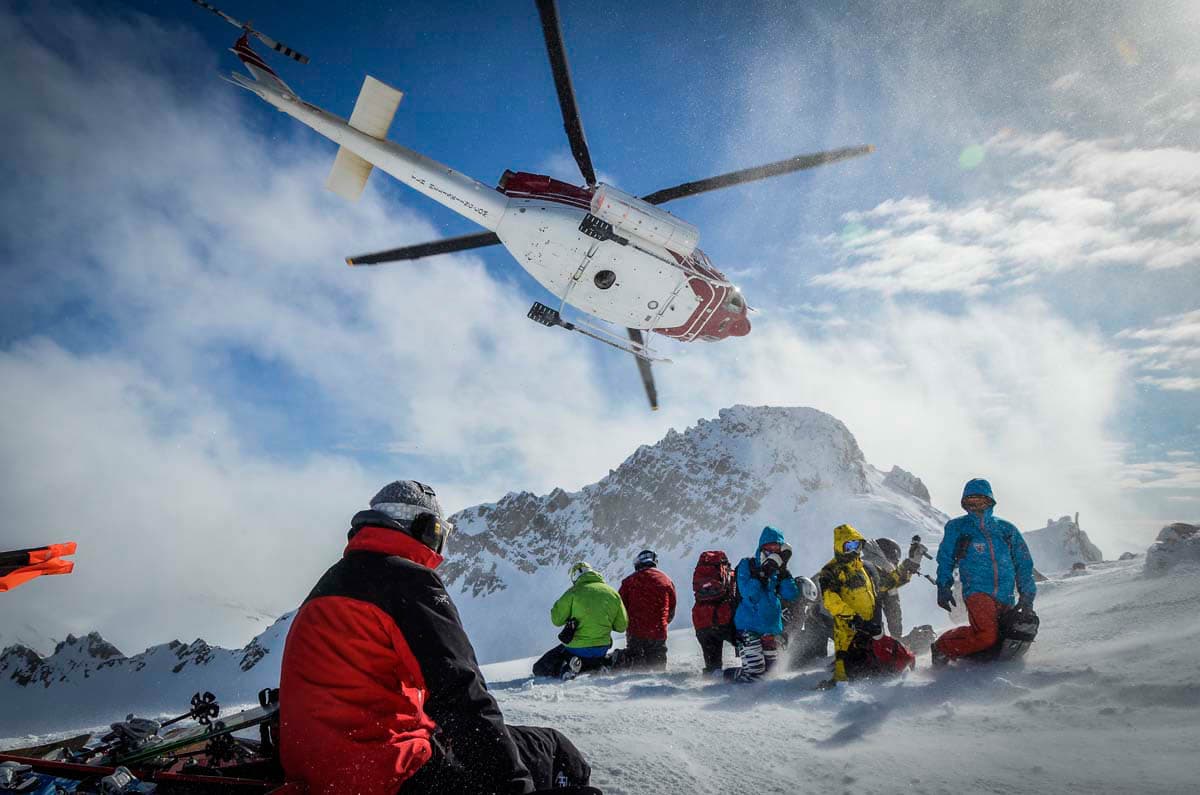 A skier enjoying the winter sports scene at Tyax Heliskiing in Vancouver, surrounded by fellow skiers at a ski resort, with a ski lift visible in the background.
