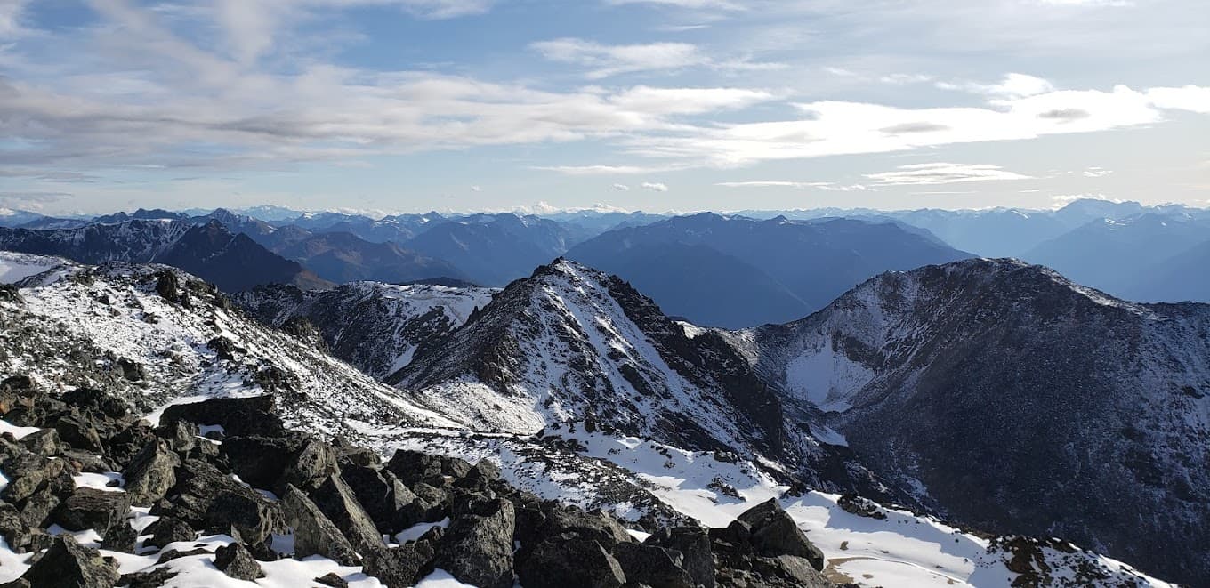 Scenic view of the rugged mountains at Tyax Heliskiing in British Columbia, Canada. A cozy chalet is nestled among the snowy peaks, suggesting a vibrant winter sports scene.